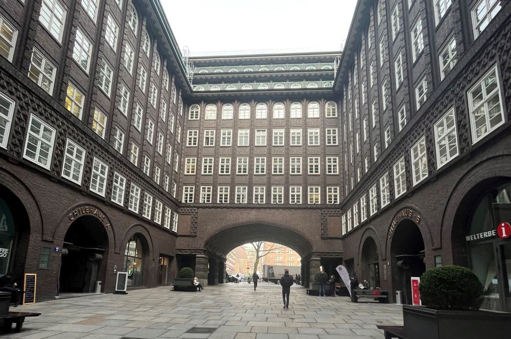 A large rectangular courtyard, with many stories of rather plain windows set close together and brick walls between. At the opposite end of the courtyard is a wide archway.