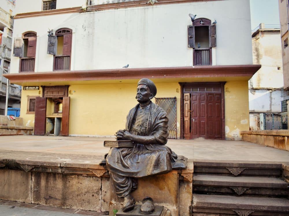 At Kavi Dalpatram Chowk, a statue of a man, sitting, one leg tucked under him, his shoe sitting on the ground next to his other foot.