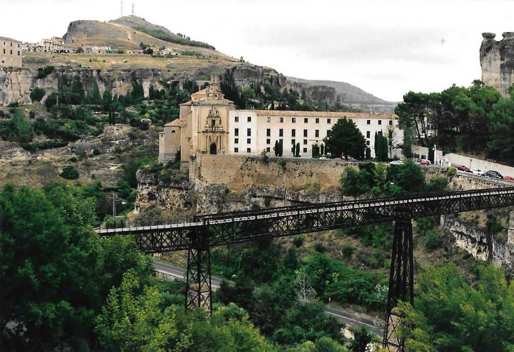 Looking across a gorge, a walking bridge extends across the gorge right to left, and beyond it on the other side is an elegant wide building of 4-5 stories.