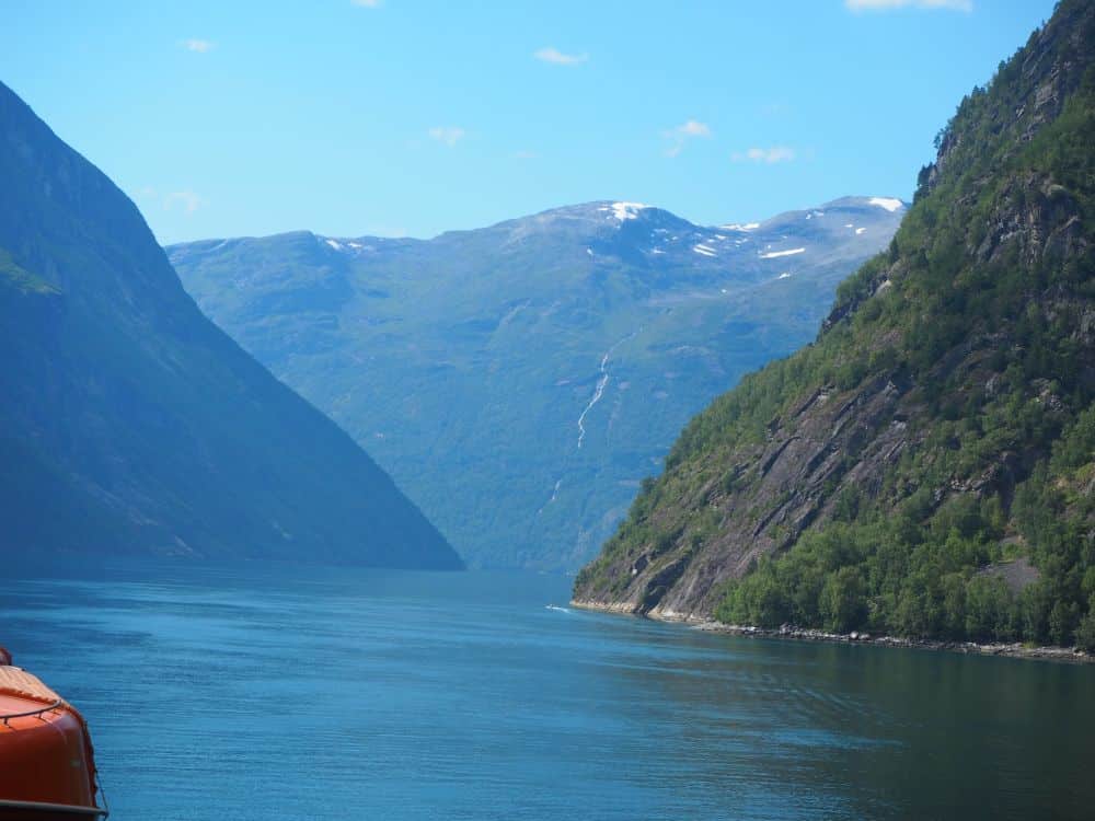 The entrance to Geirangerfjord. Steep hills on either side, and big mountains in the background.