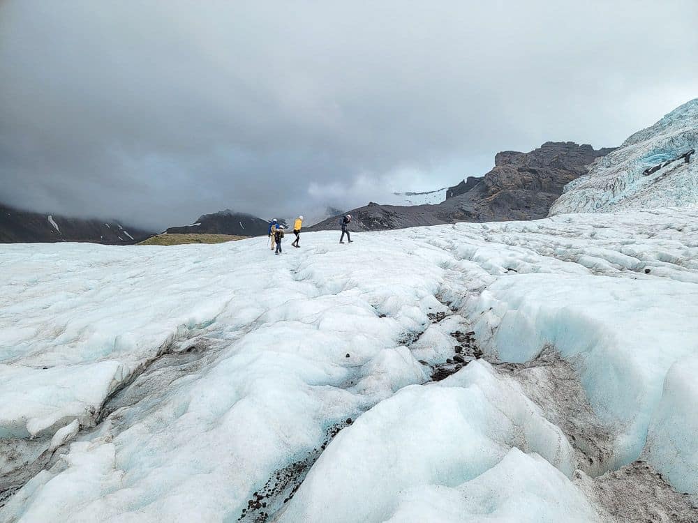 An expans of ice with, in the distance, a few hikers.