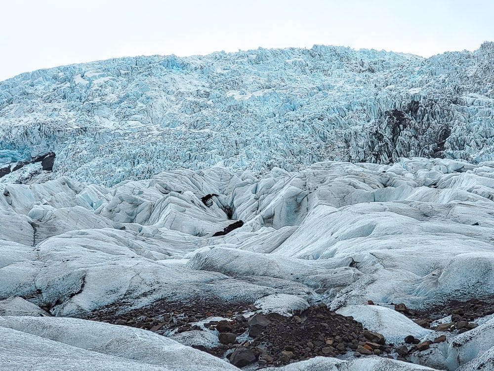 A view of an ice-covered hill: it looks jagged, and the ice on the upper parts of the hill is blue-tinted.