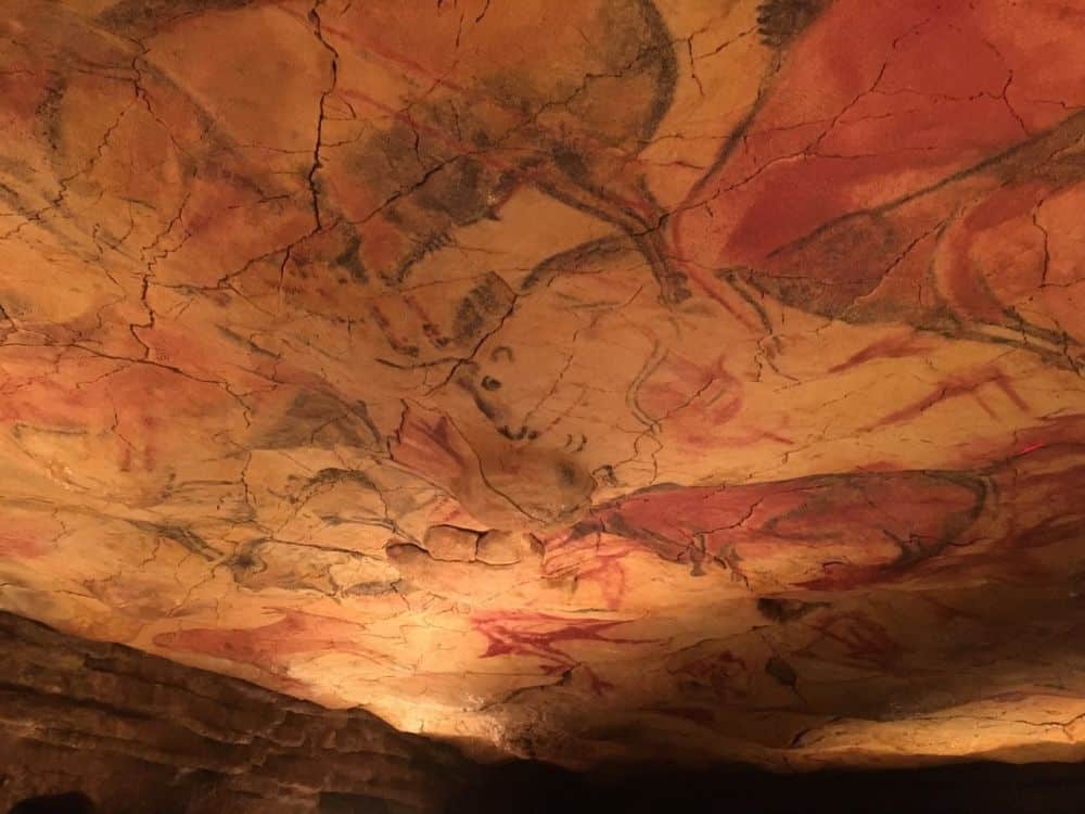 A stone surface - ceiling - with several images of bulls on it in shades of grey and red.