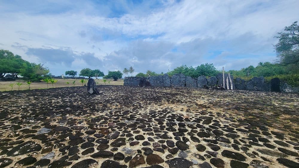 A marea with black paving stones on the ground, a wall of standing stones at the far end.