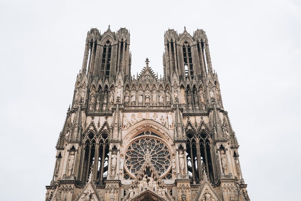 Looking up at the front of the cathedral: two square towers, very lacy with many vertical gothic openings, rose window at the center above the central entryway, lots of statue niches with figures and also gargoyles.