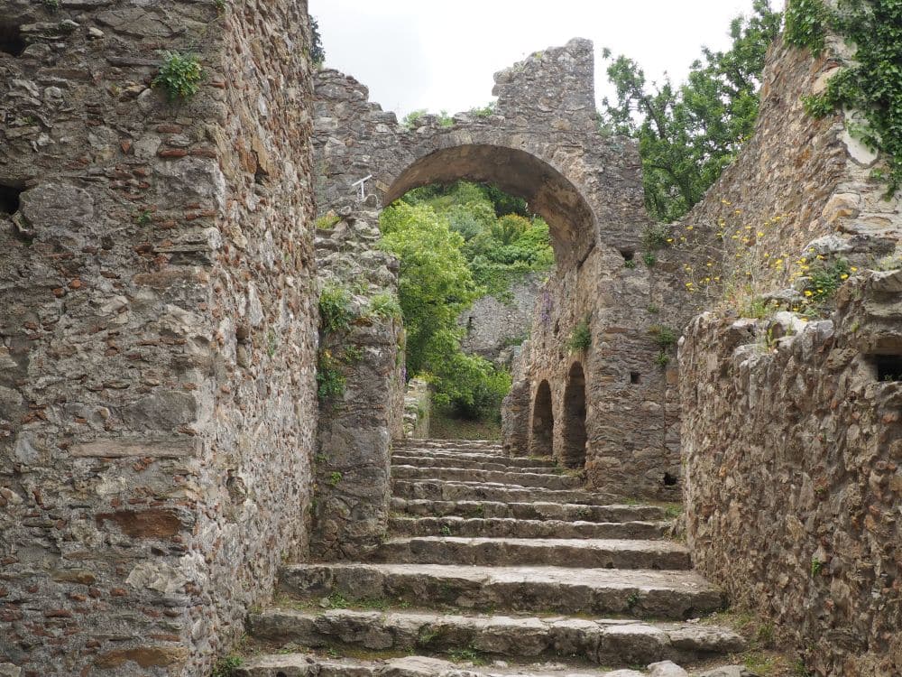 Looking up a gradual stairway of stone, with partly ruined stone walls on either side and an arch across it.