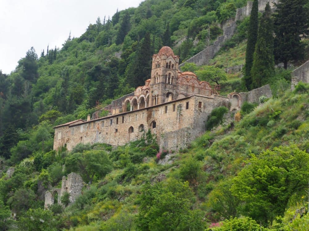 On the side of a hill, a stone building with a square tower, surrounded by a low stone wall.