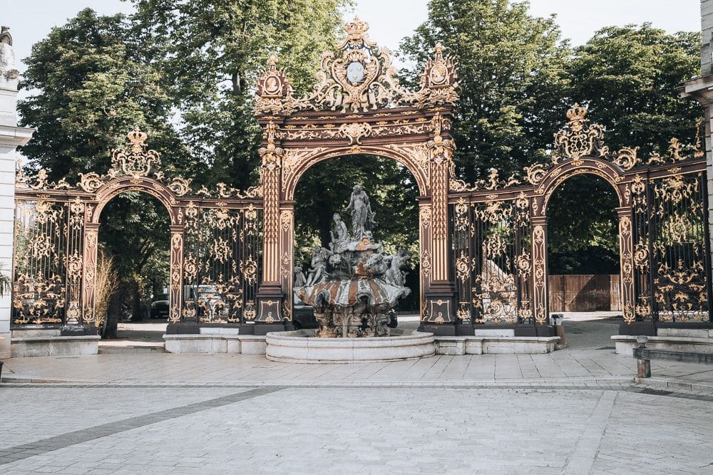 Extremely ornate triple gateway with an equally ornate fountain centered in front of the gateways.