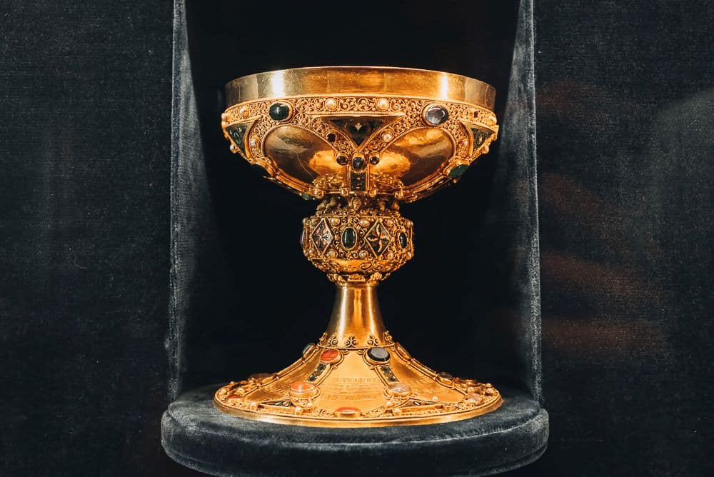 A gold chalice with lacy decorations around the cup, handle and base and gems inset into it.