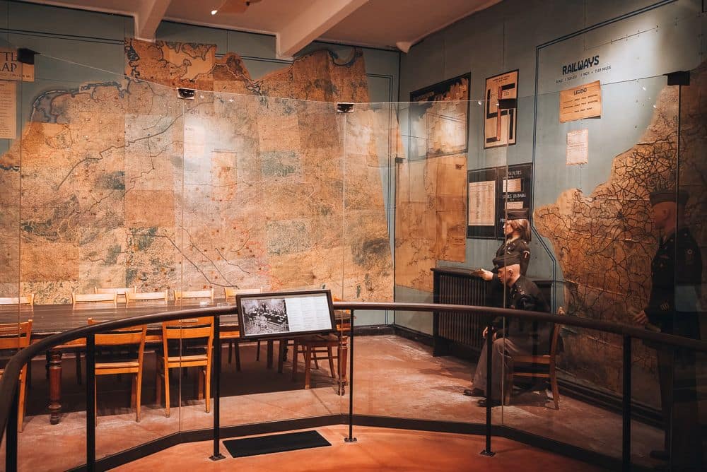 A room with a table and a sideboard and walls covered in maps. The table and map walls are blocked off to visitors by a rail.