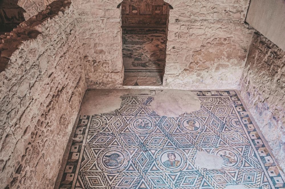 View of a corner of a room with two walls and one doorway; the floor is covered in a geometric-patterned floor, mostly triangles, but with circular sections with images of people or animals.