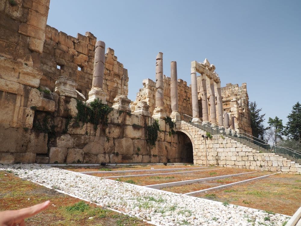 Seen from a ways to the side, the portico has a row of pillars, most damaged, and a stairway going up to them.