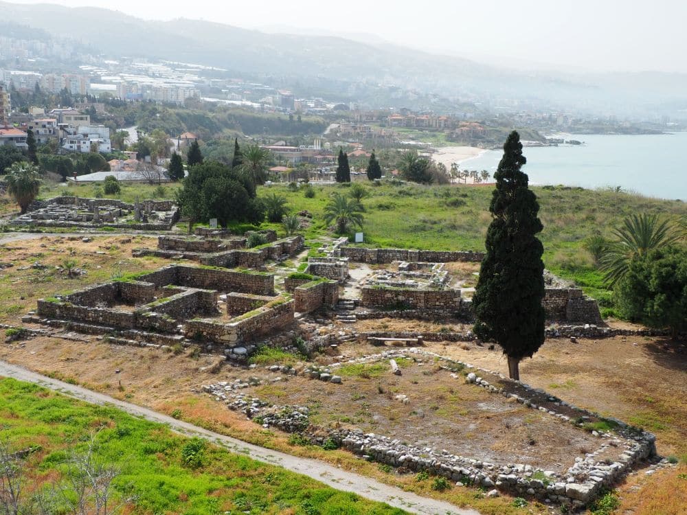 Big view of gentle hills down to the sea on the right. In the foreground, low stone walls show where several buildings were.