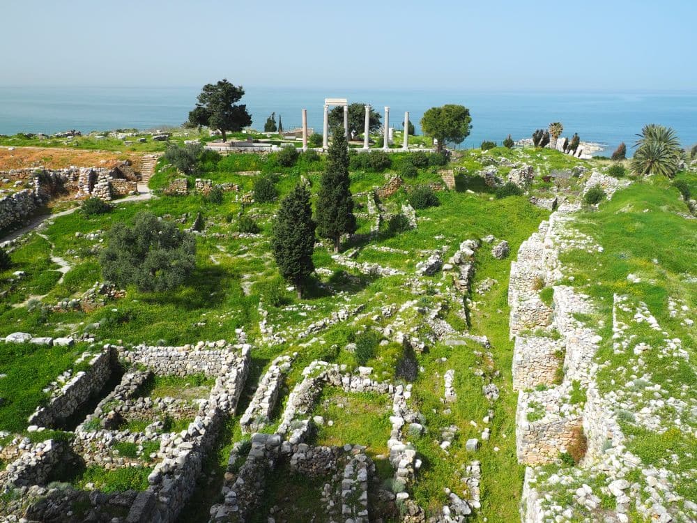 Various low walls indicating the shapes of buildings, a much thicker wall on the right and a few Roman-era columns in the background. Beyond that, the sea.