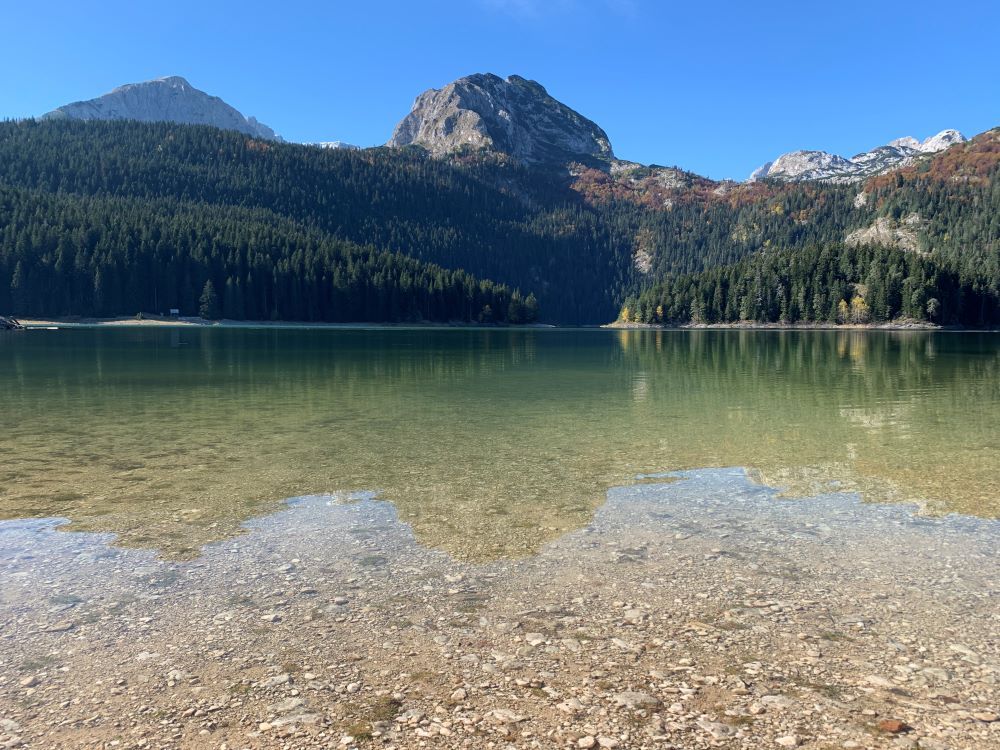 Seen from water level, a lake with clear water and a round-topped mountain on the other side of the lake.