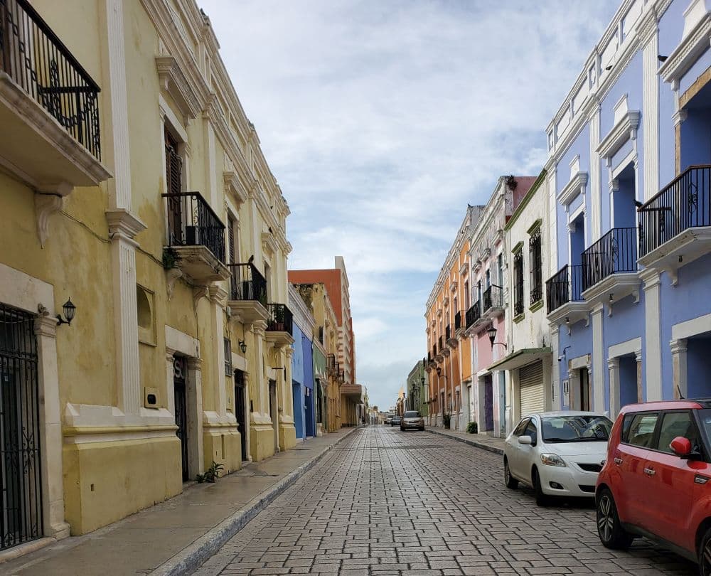 A city street lined with two-three story buildings. They are in various pastel shades.