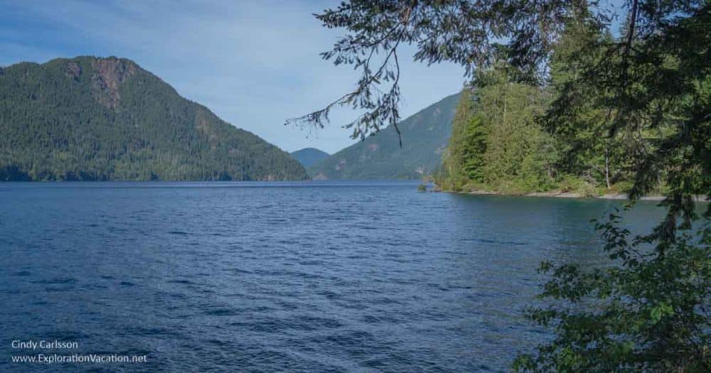 View of a lake seen from its shore - blue water, green hills sloping down to the water.