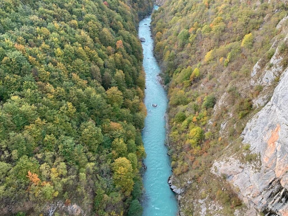 A river with very blue water flowing through a deep cut between 2 hills.