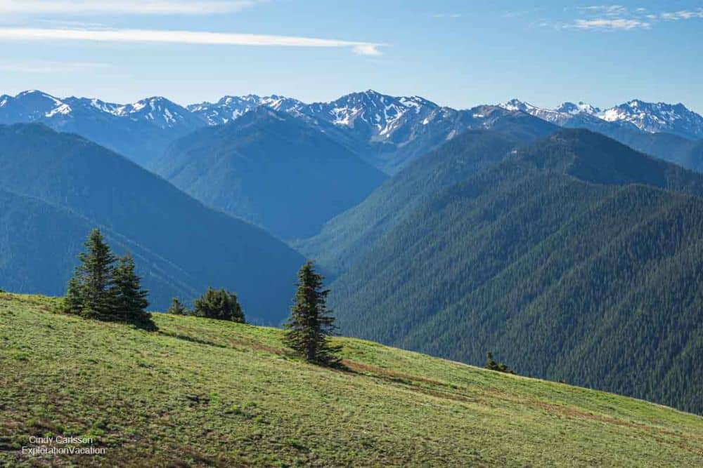 A big view from a mountain toward a ridge of mountains, which have snow near the tops.