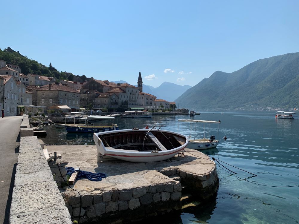 Foreground, a rowboat pulled up on a sea wall. Beyond a cluster of stone buildings along a shoreline.