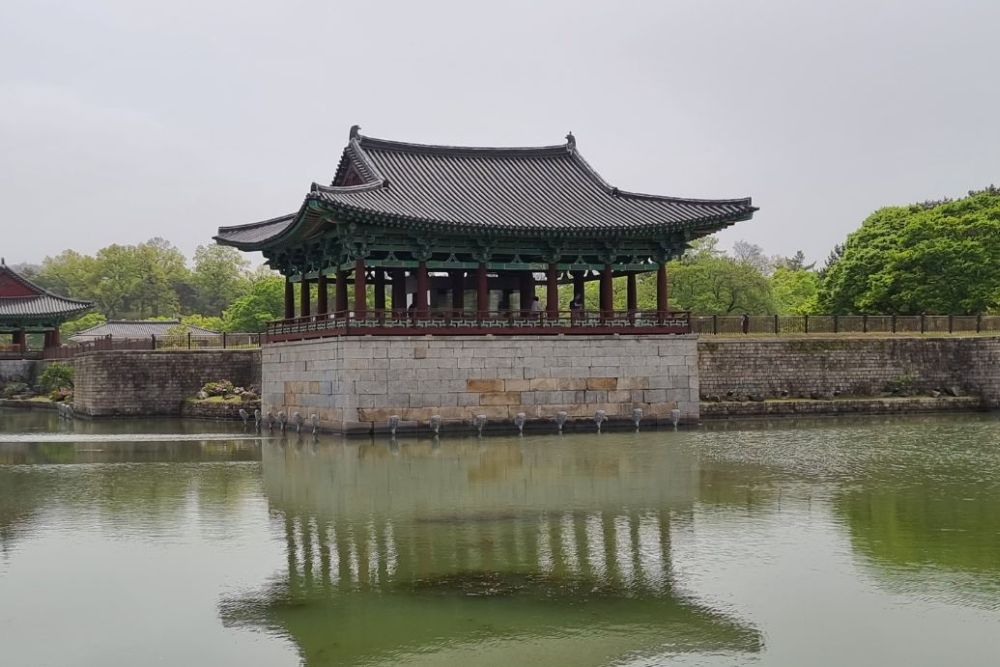 A small open-sided building on the edge of a pond.