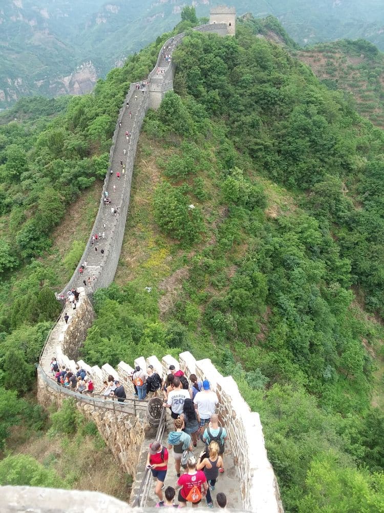 A view along a length of the wall looking from one peak (and guard tower) toward another. A group of people going down the stairs along the top of the wall.