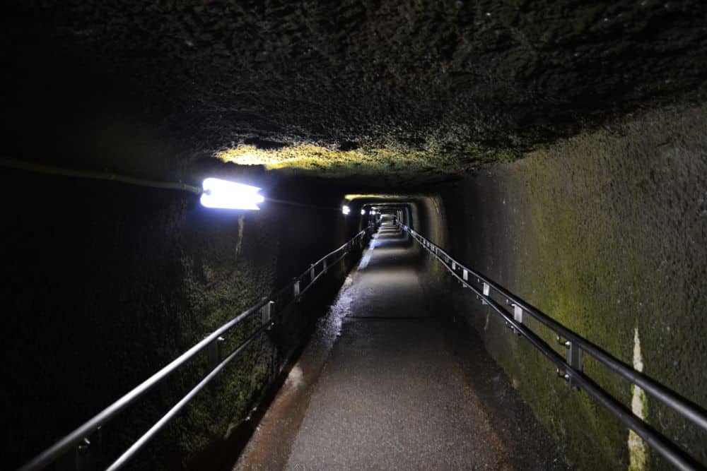 A long straight mine tunnel with a low ceiling and handrails on both sides.