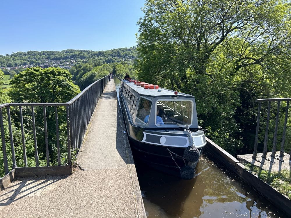 Looking down the footpath and the canal, but there is a long narrow canal boat that fills the width of the canal.