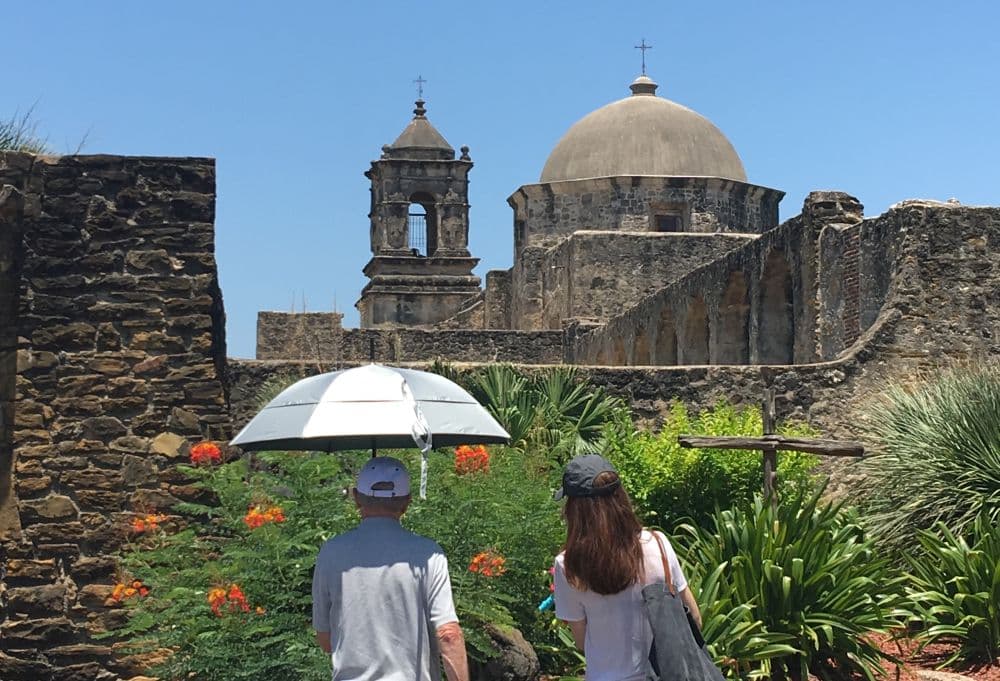 Two people stand, backs to camera, looking at the dome and bell tower of San Jose Mission
