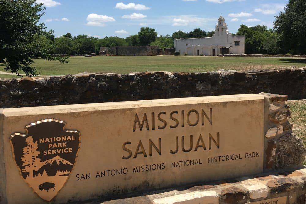 Sign reading Mission San Juan: San Antonio Missions National Historical Park. Behind it, the white mission building with bell tower.