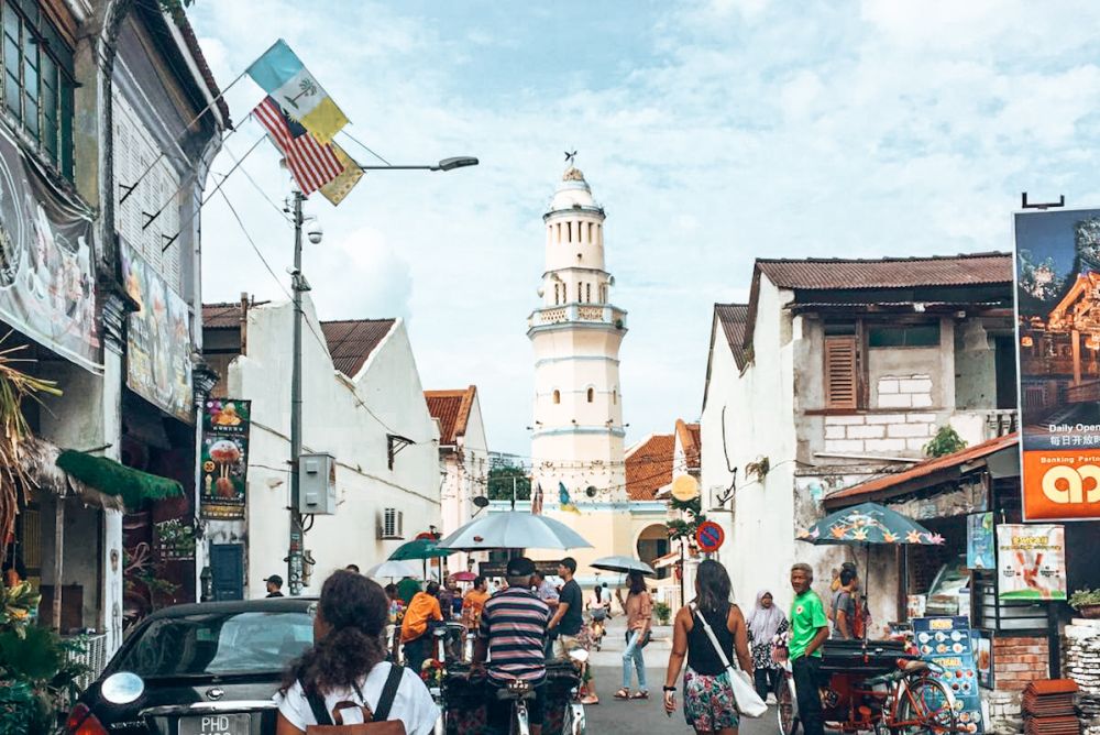 View down a street busy with pedestrians, with a tall round tower in the background.