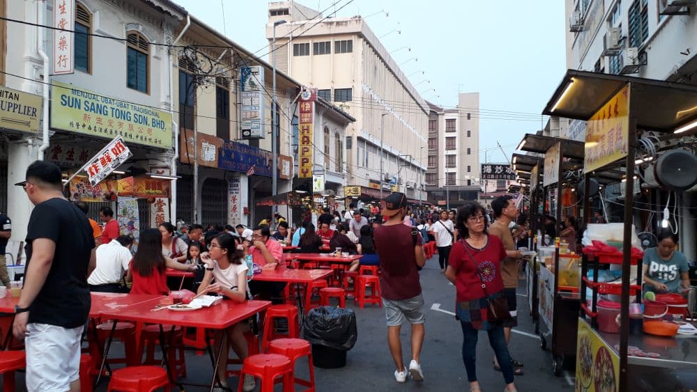A pedestrian street with red tables and chairs and people eating.