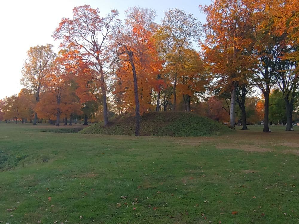 Trees in fall colors around an earthen mound.