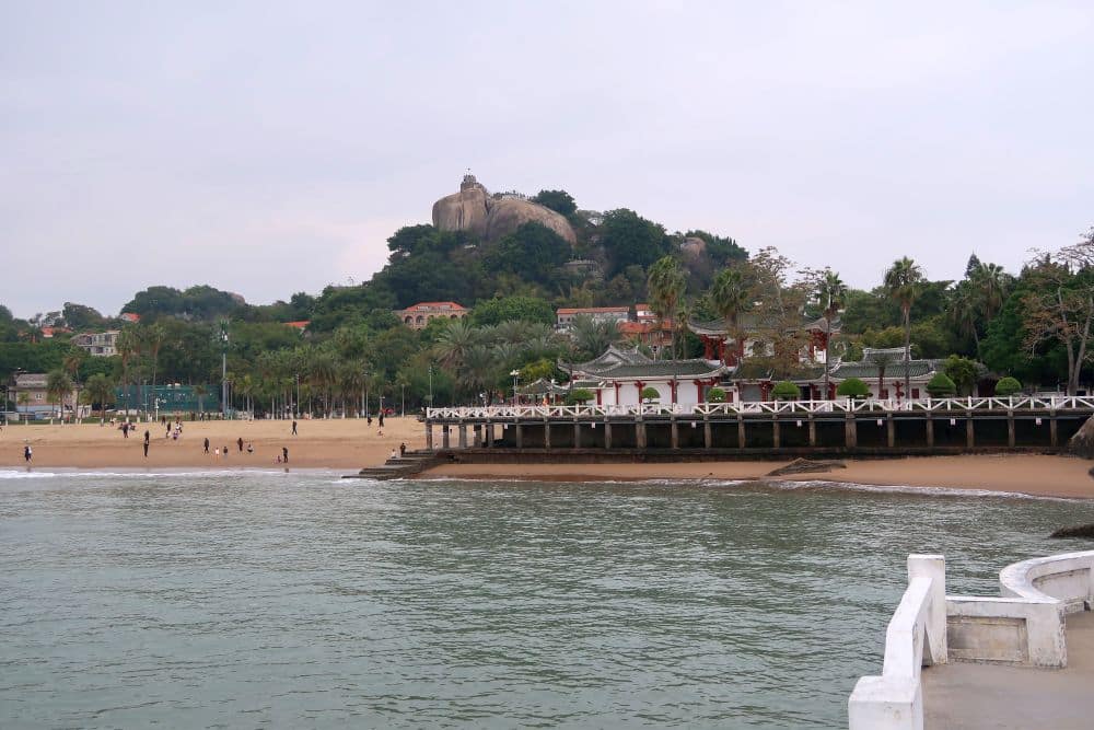 A building on a hill overlooking a beach and a pier.