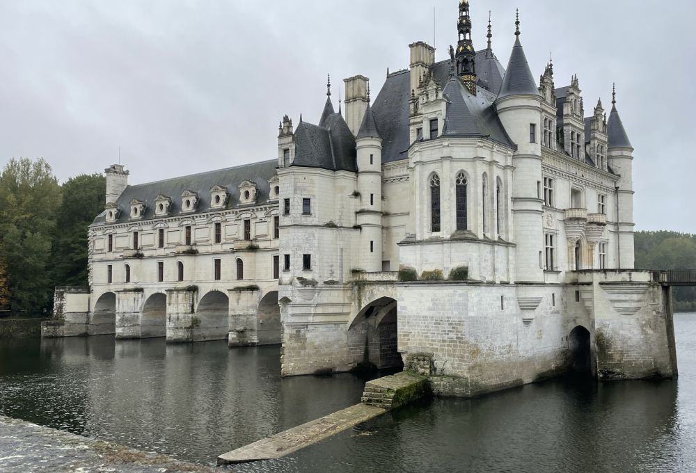 A white castle with many turrets, set on a series of arches over the Loire River.