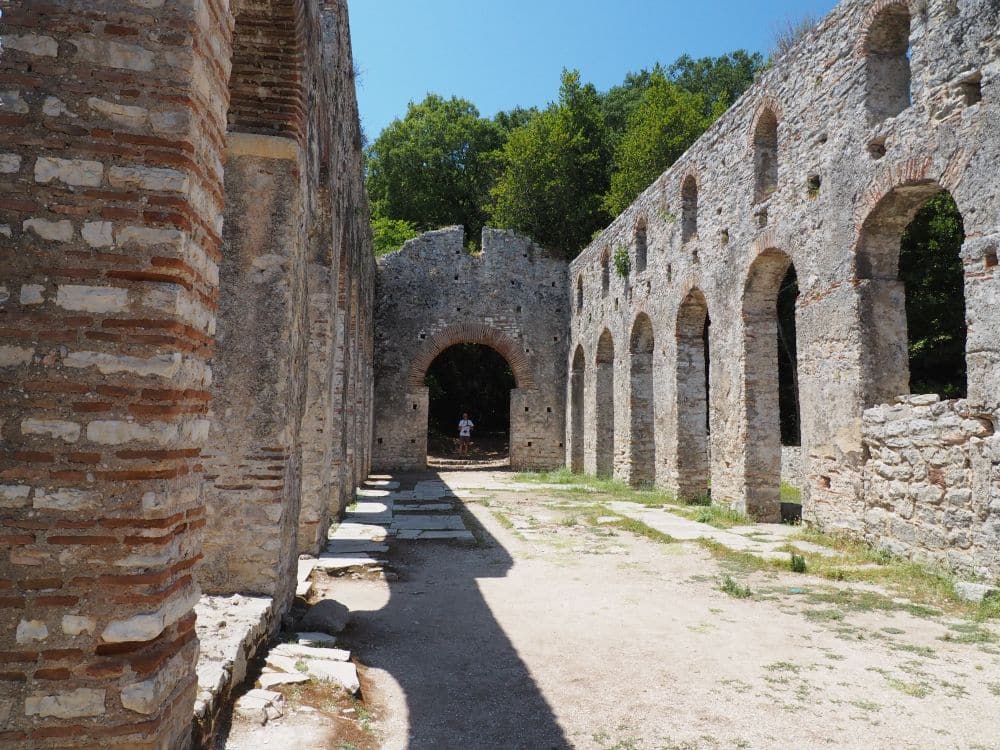 Looking down a ruined church with intact walls but no ceiling. Walls in stripes of stone and brick, archways along both sides.