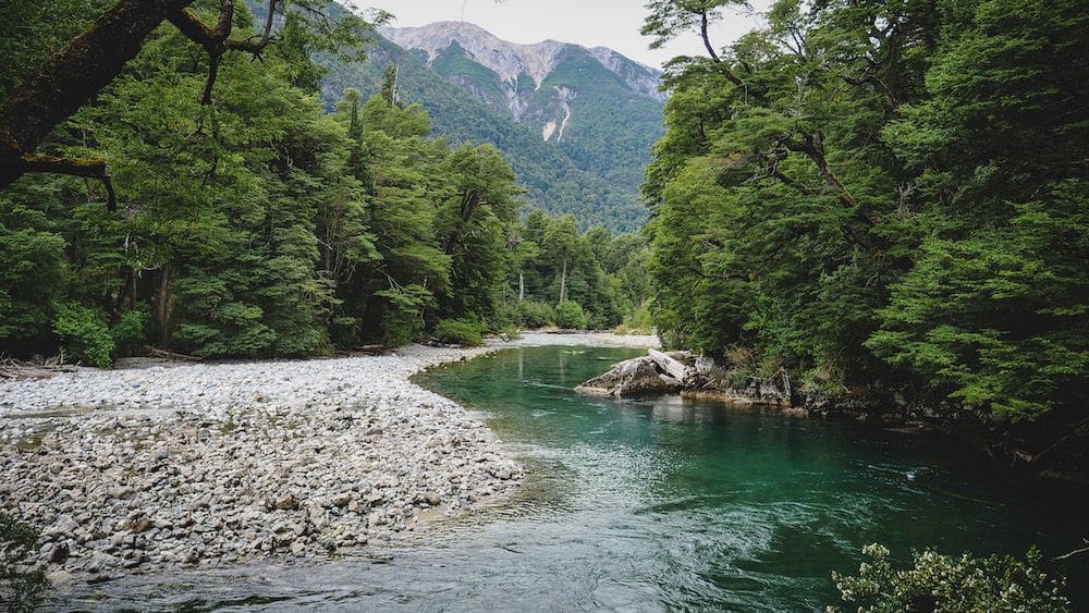 A narrow river winds out of sight between forested shores, mountains in the background.