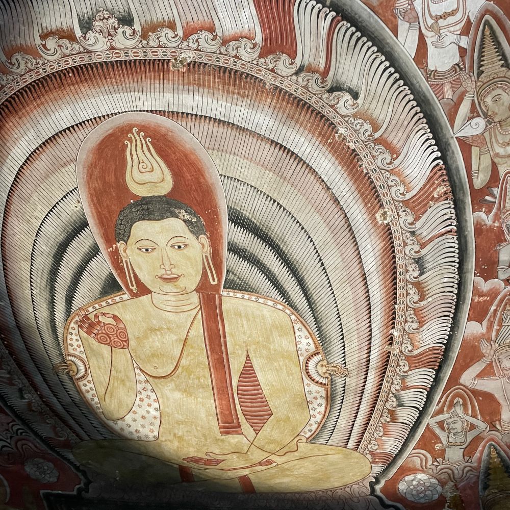 An image on a fresco, lit by flashllight, of a seated Buddha.