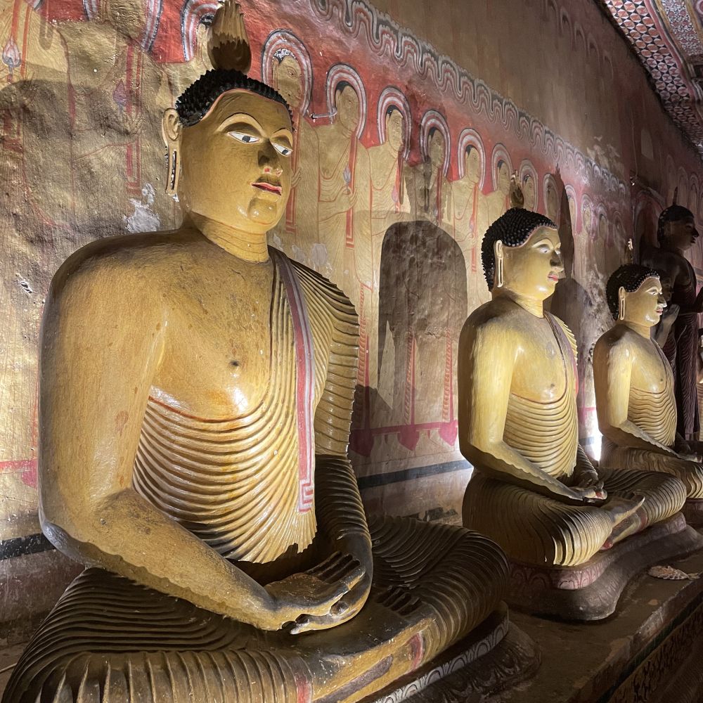 A row of seated Buddha statues - bas-reliefs against a painted wall. The statues are partially painted too.