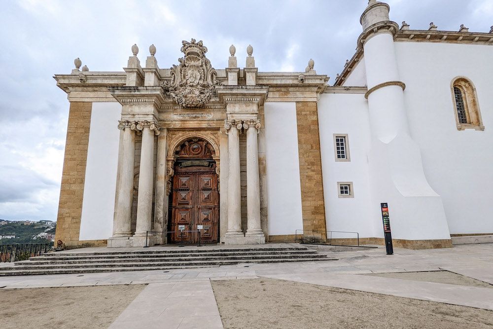 A white building with an ornate doorway, flanked by double pillars in a baroque style.