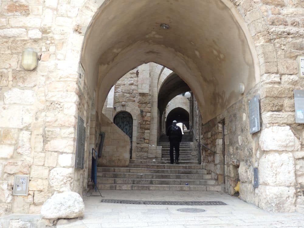 An archway covering a street that is really a stairway. A man in a kippah walks up the steps.