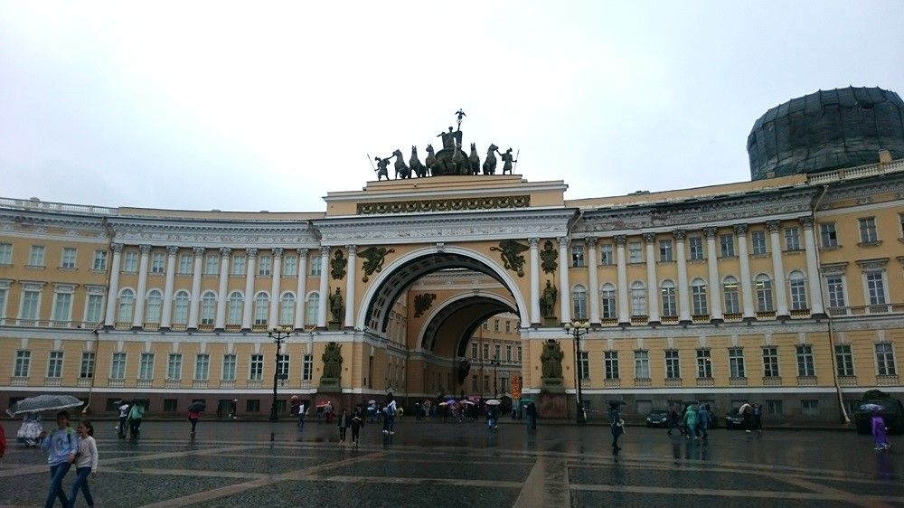 A large archway in a curved building with baroque statuary on top of the arch.