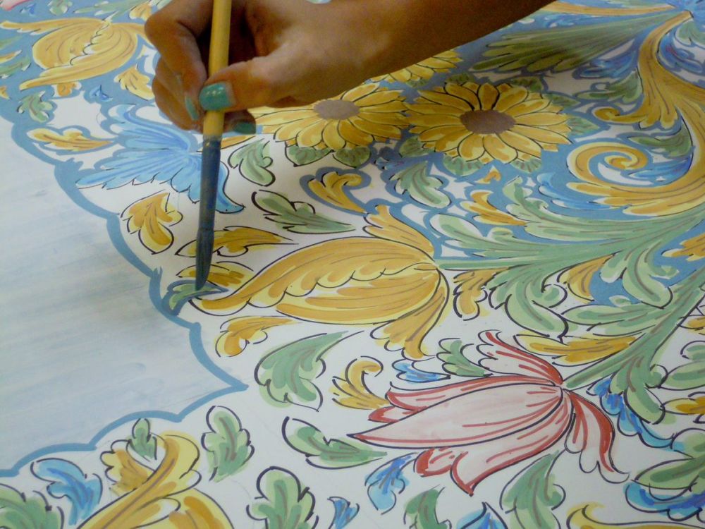 A person's hand holding a brush, painting a flowery tile pattern.