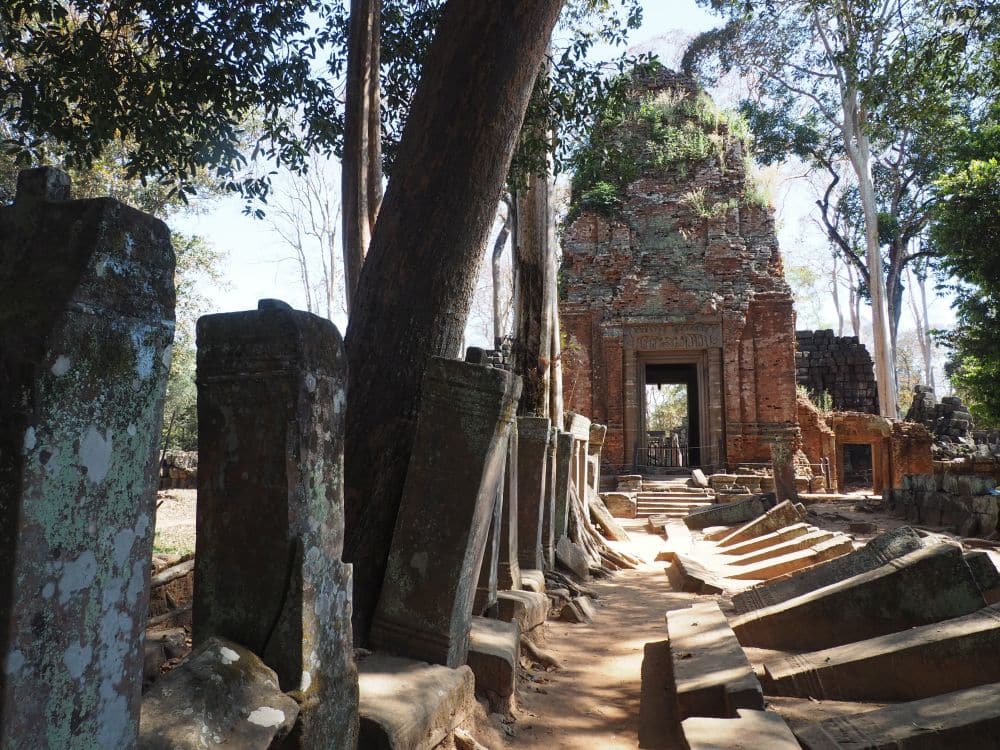 A path leading to a small conical temple. The path has standing stones along the left and fallen stones along the right.