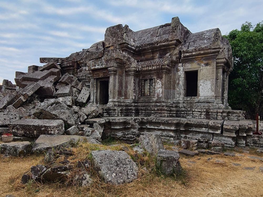 A temple built of stone where the front part is intact, including a roof, bu tthe back end is a pile of very large rubble.