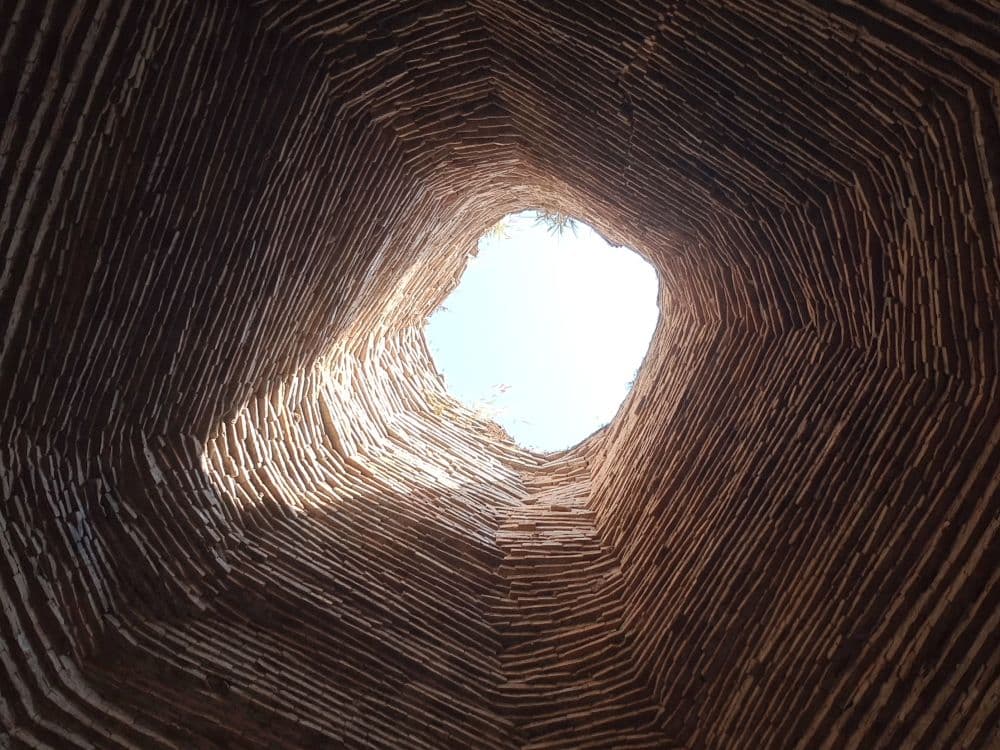 A hole in the ceiling lets light it that shows the rows of bricks up the sides of the walls.