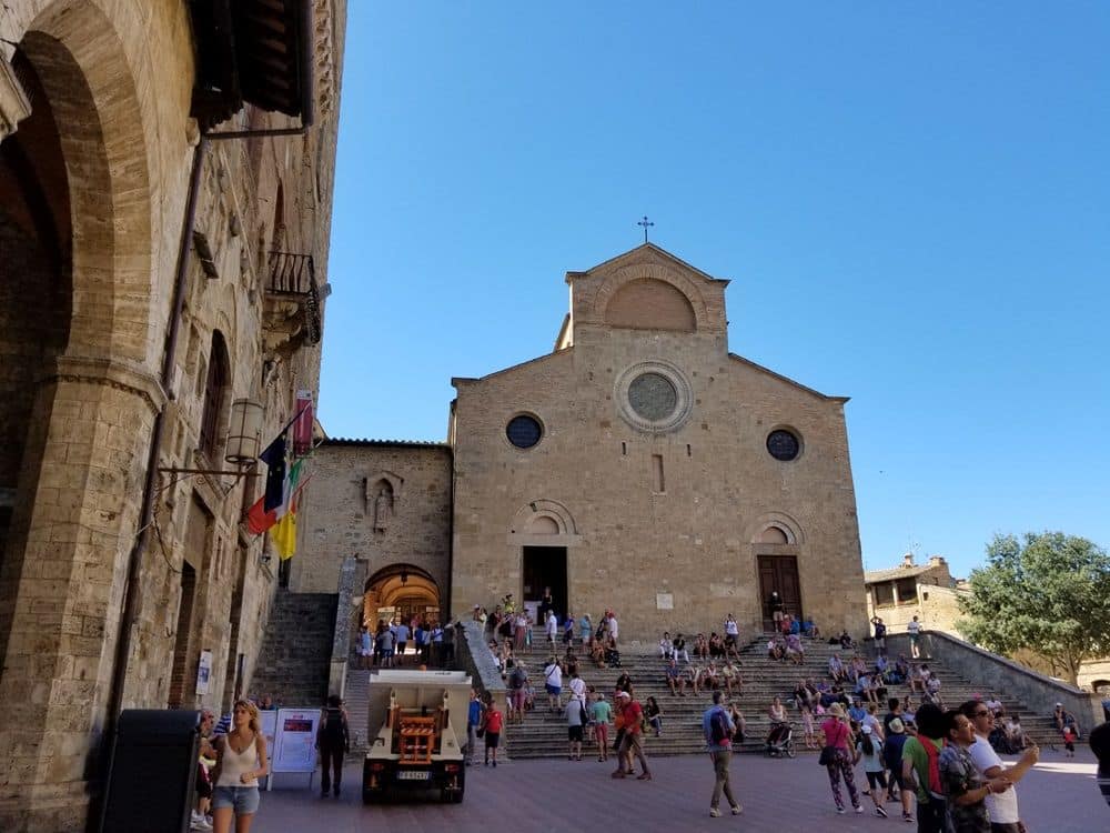 A plaza with a flat-fronted Romanesque church at the far end, with people sitting and standing on the steps.