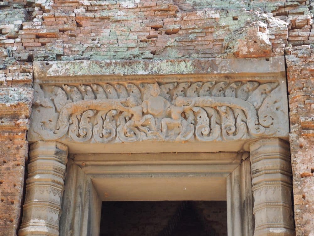 A doorway topped with bas-relief with small human/god figures and leafy detail.
