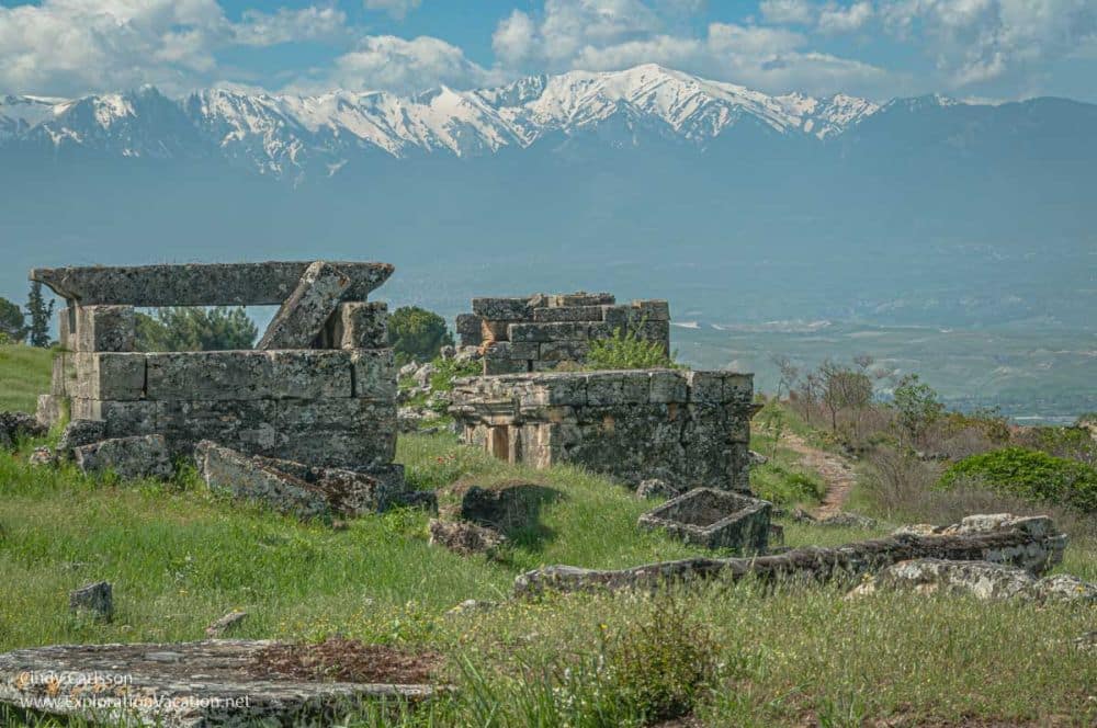Several ruined stone structures with snow-capped mountains in the background.