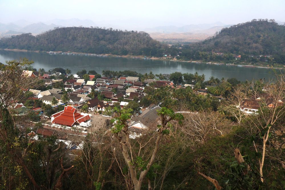 View over a low-rise town of Luang Prabang with river beyond and hills beyond that.